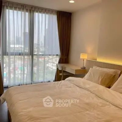 Cozy bedroom with city view, featuring a comfortable bed and a small desk by the window.