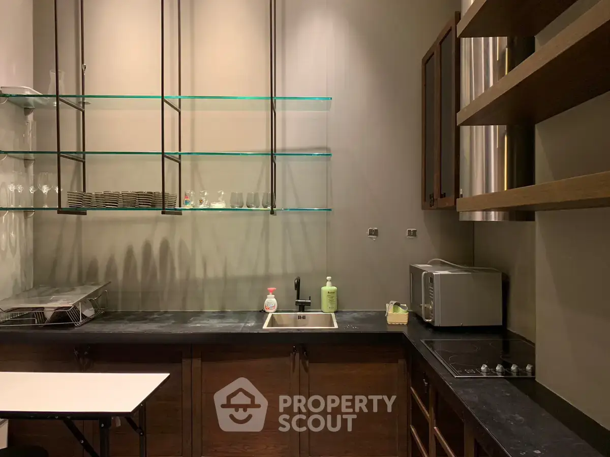 Modern kitchen with sleek design, featuring glass shelves, dark countertops, and stainless steel appliances.