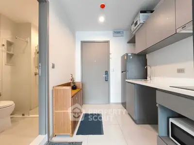 Modern apartment entryway with sleek kitchen and bathroom access, featuring contemporary appliances.