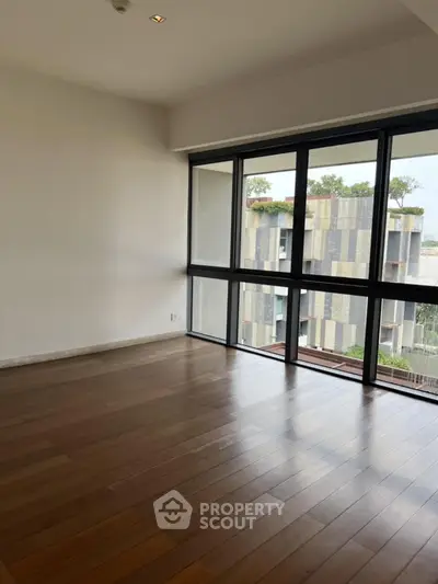 Spacious empty room with large windows and wooden flooring, offering a serene view.