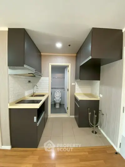 Modern kitchen with dark cabinets and open layout leading to a compact bathroom.
