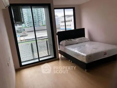 Modern bedroom with large window and city view, featuring a comfortable bed and sleek flooring.