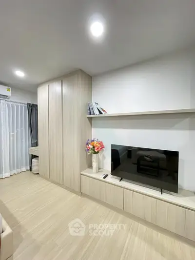 Modern living room with built-in cabinets and large TV, featuring elegant decor and bright lighting.