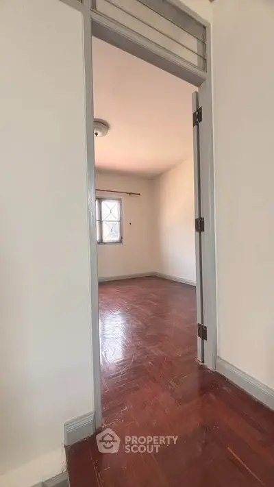 Spacious empty room with wooden flooring and natural light through window.