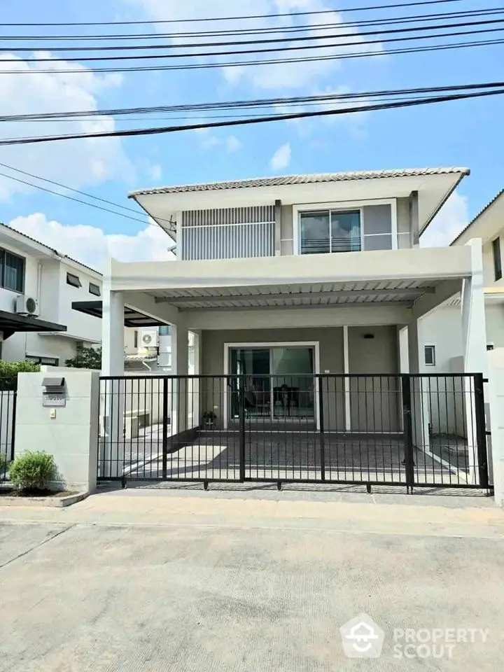 Modern two-story house with gated entrance and spacious driveway in suburban neighborhood.