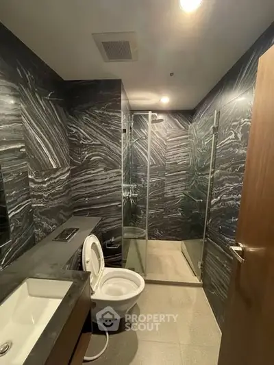 Luxurious modern bathroom with sleek black marble walls and glass shower enclosure.