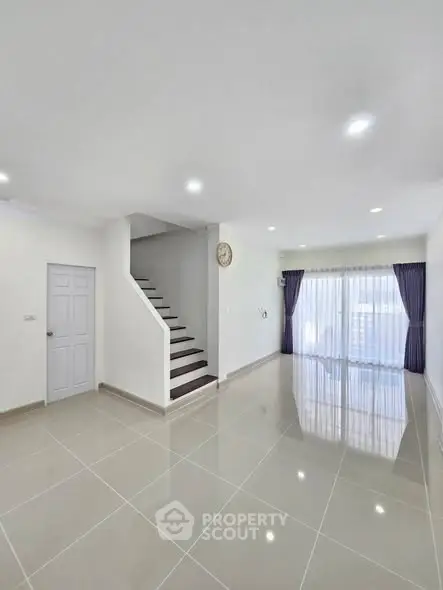 Spacious modern living room with glossy tiled floors and staircase, ideal for family gatherings.