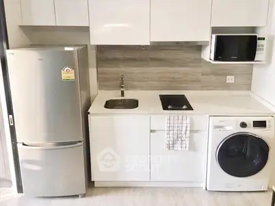 Modern kitchen with sleek appliances including fridge, microwave, and washing machine in compact layout.