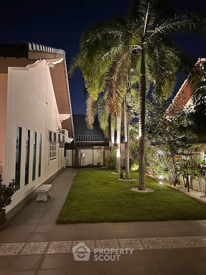 Charming night view of a tropical garden with palm trees and elegant exterior lighting.