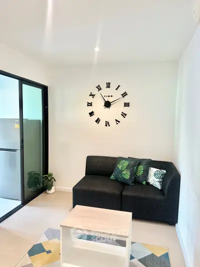 Modern living room with stylish black sofa, wall clock, and glass door leading to balcony.