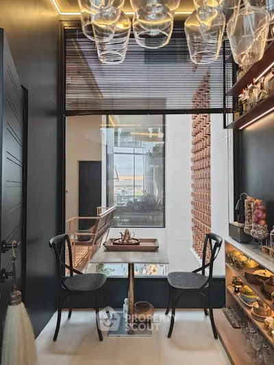 Chic urban kitchenette with modern design, featuring unique overhead glass storage, sleek surfaces, and a cozy dining nook with a view.