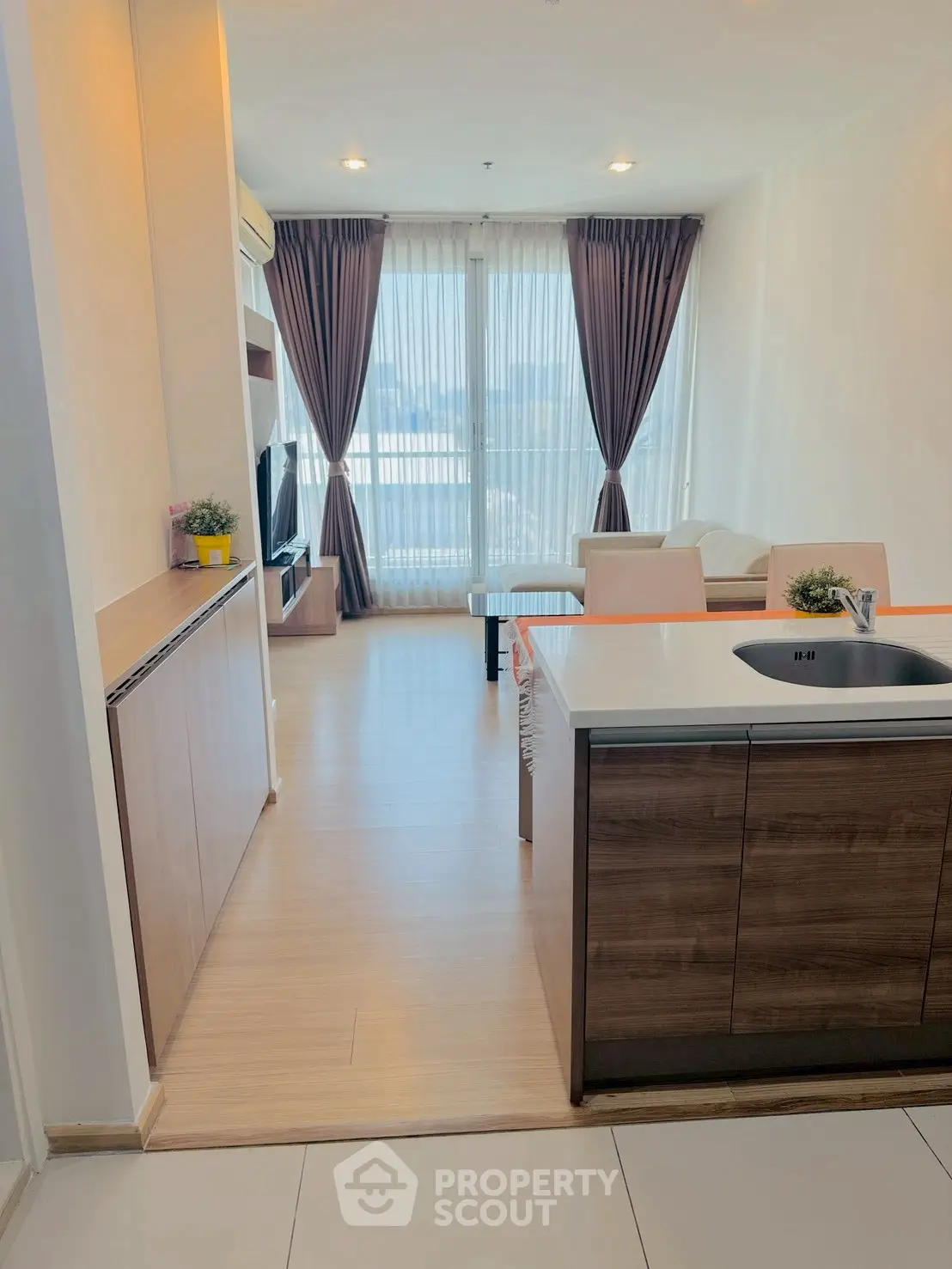 Modern open-layout living room with kitchen, featuring large windows and stylish decor.