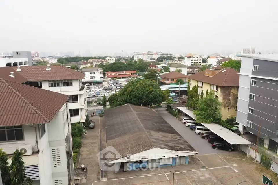 Aerial view of residential buildings with parking area and cityscape in the background.