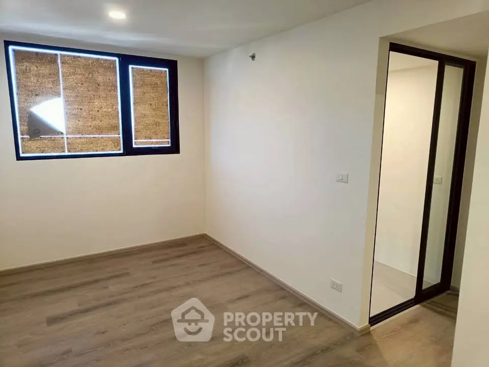 Spacious empty room with wooden flooring and large window, perfect for customization.