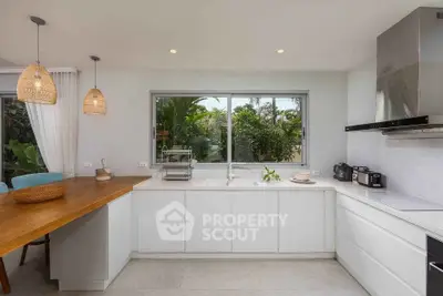 Modern kitchen with white cabinets, large window, and wooden breakfast bar in tropical setting.
