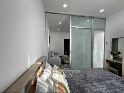 Modern bedroom with sliding glass doors leading to a cozy living area, featuring stylish decor and ample natural light.