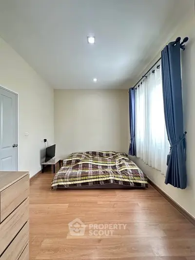 Cozy bedroom with wooden flooring and natural light from large windows.