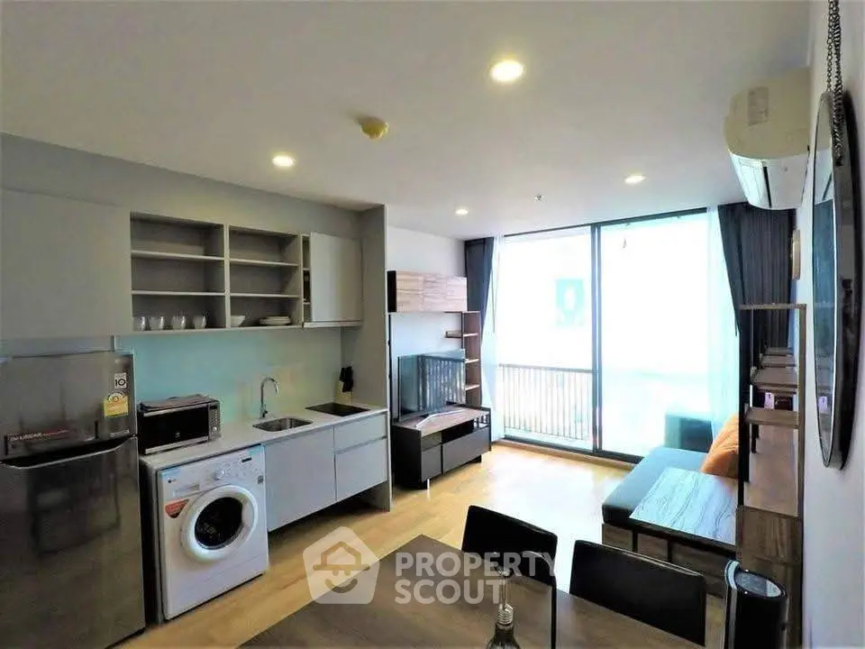 Modern open-plan living room with kitchen, featuring washing machine and balcony access.