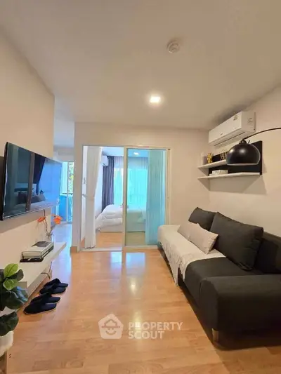 Modern living room with sleek sofa, wall-mounted TV, and view into cozy bedroom.