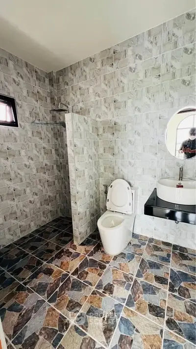Modern bathroom with tiled walls and floor, featuring a round mirror and sleek fixtures.