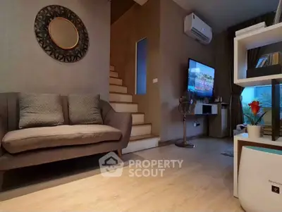 Cozy living room with modern decor and staircase, featuring a wall-mounted TV and air conditioning.