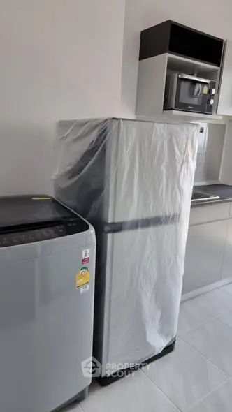 Modern kitchen with fridge, washing machine, and microwave in sleek design.