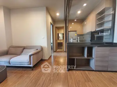 Modern open-plan living room with sleek kitchen and cozy seating area, featuring wood flooring and contemporary design.