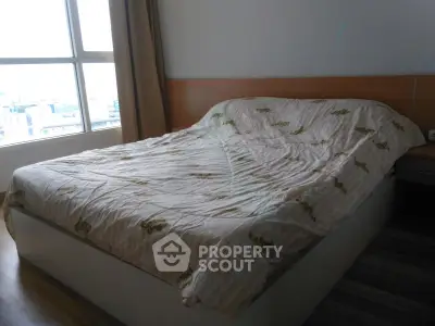 Spacious bedroom with large window offering city views, featuring a cozy bed and wooden flooring.