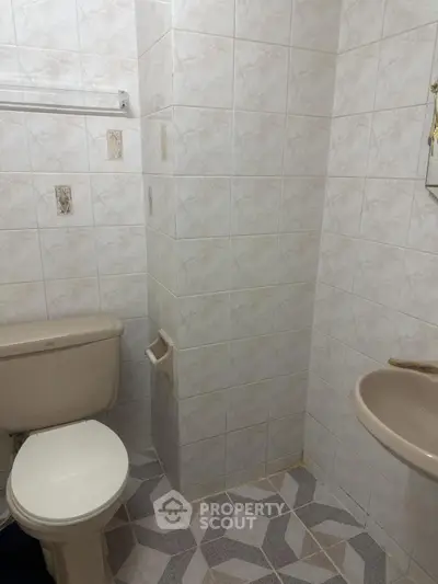 Cozy bathroom with tiled walls and floor, featuring a toilet and sink.