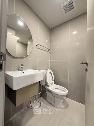 Modern bathroom with sleek design and round mirror, featuring a toilet and sink in a contemporary setting.