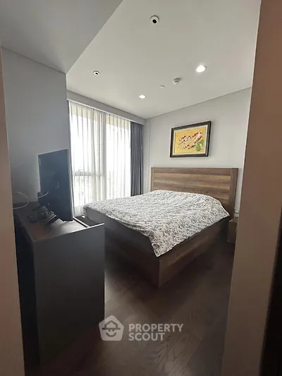 Cozy bedroom with wooden flooring and modern decor, featuring a large window for natural light.