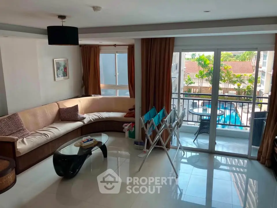 Spacious living room with large windows and balcony overlooking pool, perfect for relaxation.