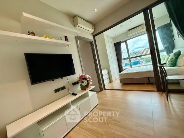 Modern apartment interior with open living room and bedroom, featuring sleek design and natural light.