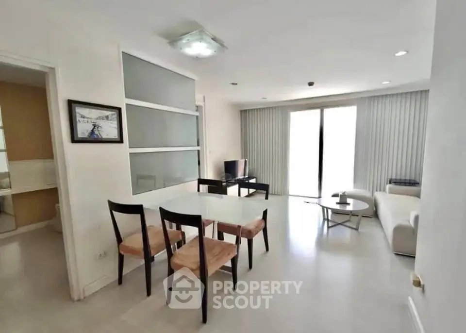 Modern living room with dining area and natural light, featuring sleek furniture and minimalist design.