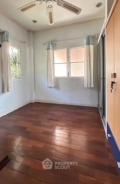 Spacious bedroom with wooden flooring and large windows for natural light.