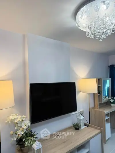 Modern living room with elegant chandelier and mounted TV, featuring stylish decor and ambient lighting.