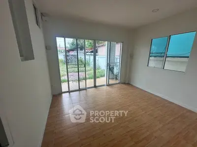 Spacious empty room with wooden flooring and large windows offering garden view.