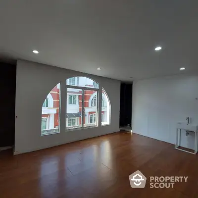 Spacious room with large arched window and wooden flooring