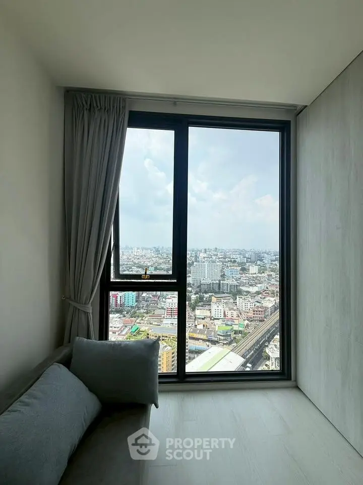 Modern living room with panoramic city view from large window, featuring sleek design and cozy seating.