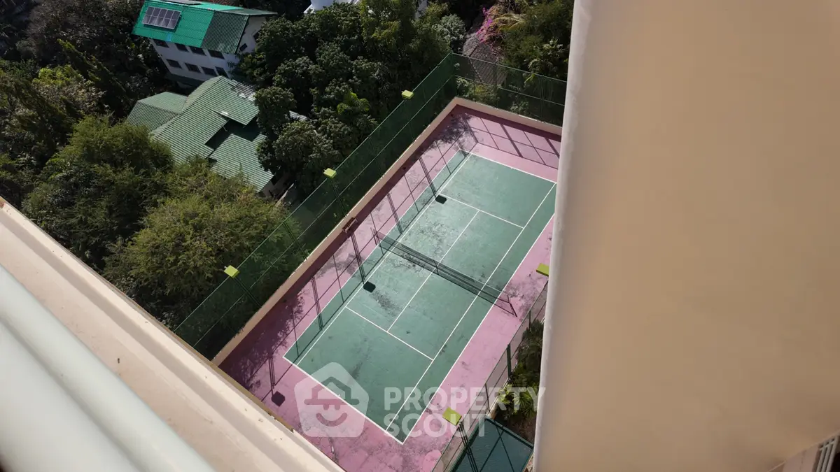 Bird's-eye view of a vibrant tennis court surrounded by lush greenery in a residential complex.