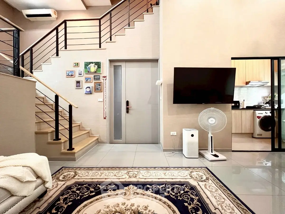 Modern living room with staircase, wall art, and open kitchen view