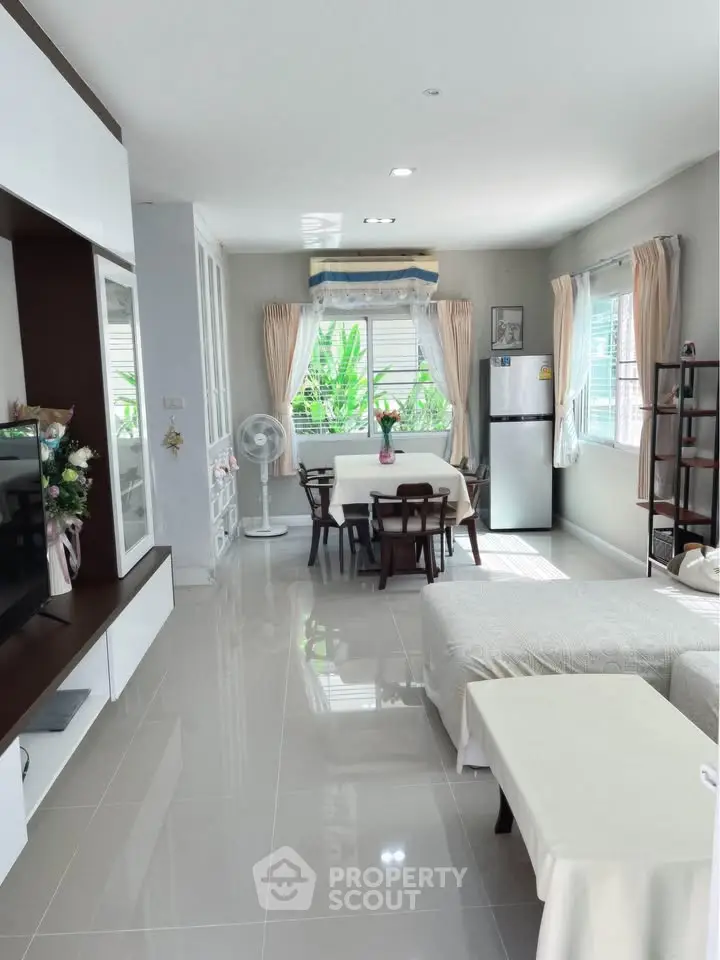Spacious living room with modern decor and natural light, featuring a dining area and sleek kitchen appliances.
