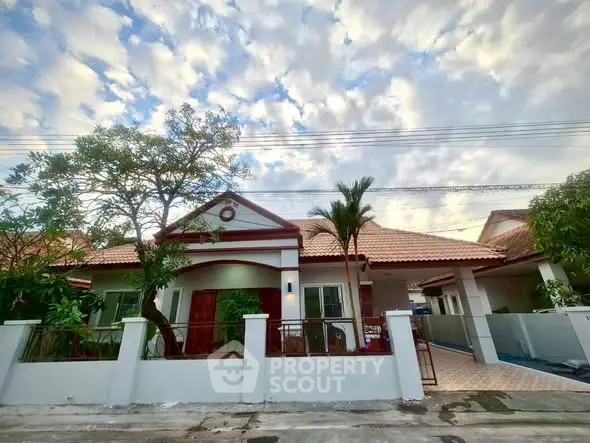 Charming single-story house with tiled roof and lush garden under a picturesque sky.