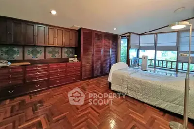 Spacious bedroom with wooden flooring and large windows offering natural light.