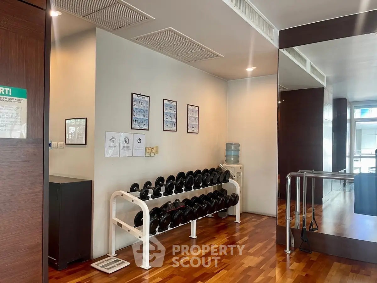 Modern gym interior with dumbbell rack and wooden flooring, ideal for fitness enthusiasts.