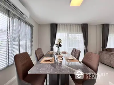 Elegant dining area with marble table, plush chairs, and large windows offering natural light in a modern home.