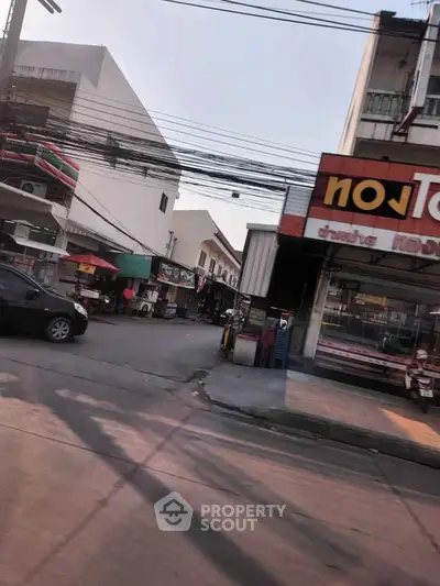 Street view of commercial buildings with shops and parked cars in a bustling neighborhood.