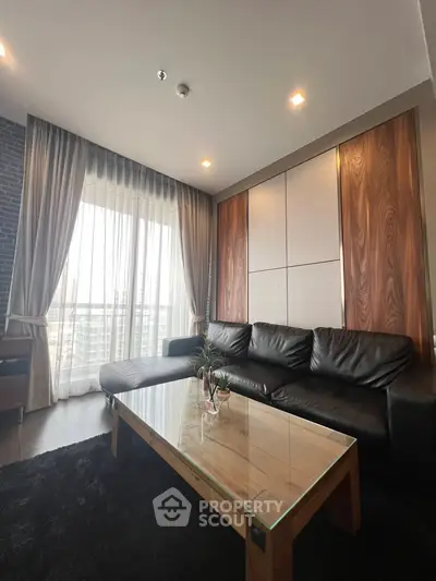 Modern living room with sleek black leather sofa and large window with city view.