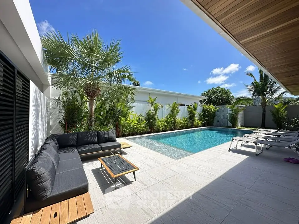 Luxurious outdoor pool area with modern seating and lush greenery under a clear blue sky.