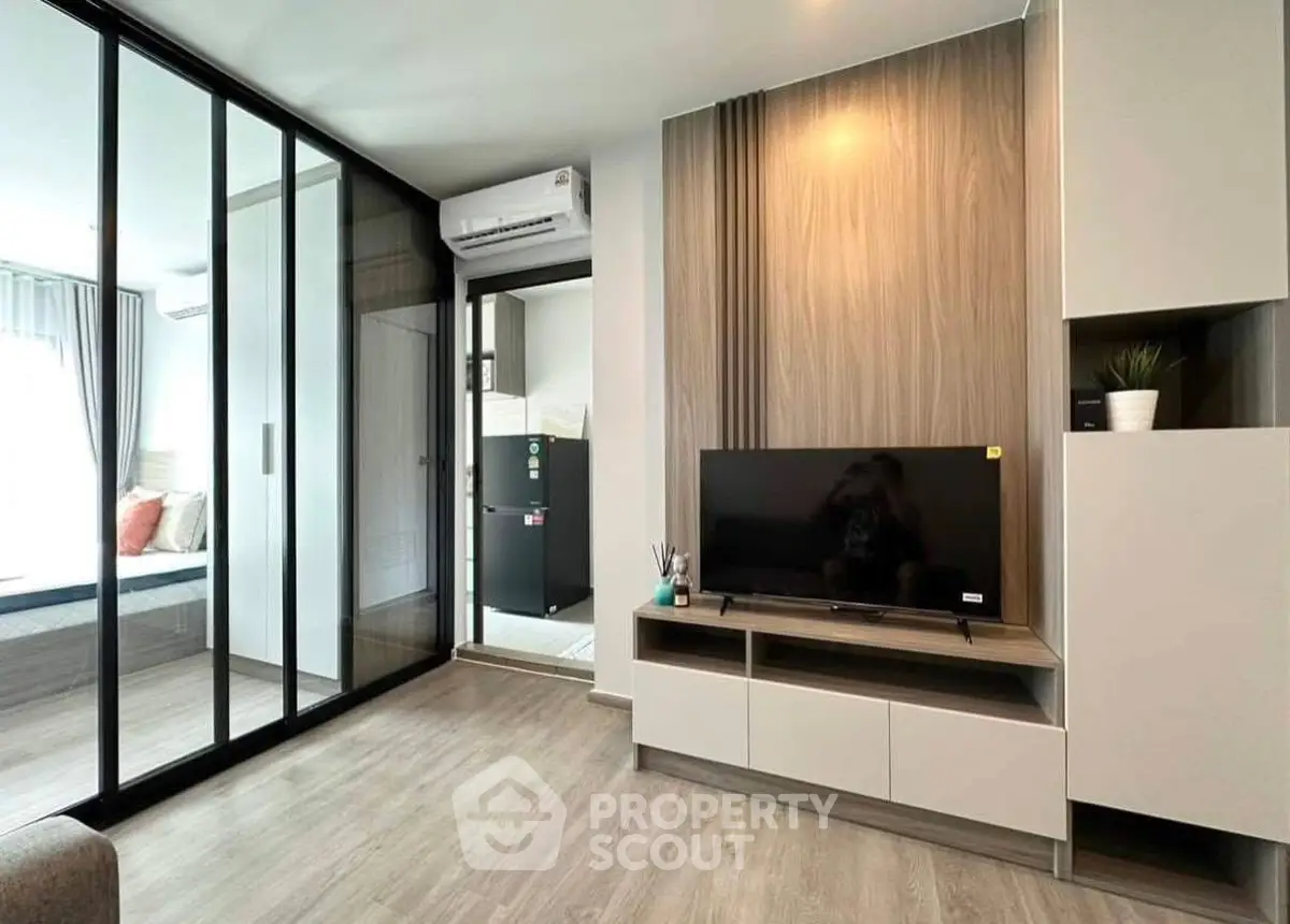 Modern living room with sleek design and glass partition leading to bedroom, featuring stylish furniture and decor.